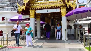 Turistler Bangkok, Tayland 'daki Wat Pho tapınağına girerler. Parlak gün ışığı dekoratif mimari ve hareketli giriş aktivitesini vurgular
