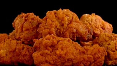 Bir el, dramatik stüdyo ışıkları altında, siyah bir arka plan ve yavaş çekim etkisiyle çıtır çıtır, baharatlı bir tavuk parçası almak için uzanır.