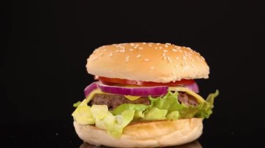 Salatalı, domatesli, soğanlı ve susamlı klasik bir sığır burger, parlak, hatta stüdyo ışıkları altında siyah bir arka planda düzgün döner.