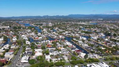 Altın Sahil banliyölerinin, sergilenen yerleşim alanlarının, su yollarının ve açık mavi gökyüzünün altındaki uzak dağların hava görüntüleri.
