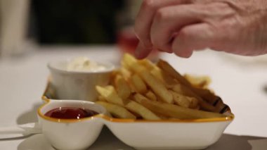 Bir el patates kızartmasına uzanıyor, onları mayonez ve ketçapa batırıyor, gevşek bir yemek atmosferine dayanıyor.