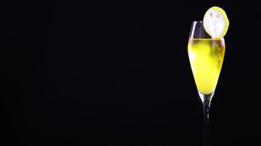 Limon dilimli bir bardakta limon ekşili kokteyl, parlak ışıklandırmalı siyah bir arka planda.