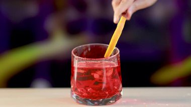 Bir Negroni kokteyli, parlak ışık altında bir bar tezgahında portakal bükümüyle süslenir.