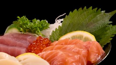 Canlı bir somon, ton balığı, deniz tarağı ve yumurtalı saşimi çeşidi limon, shiso yaprağı ve garnitür ile sunulur.