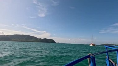 Bir tekne Phuket 'in berrak sularında yol alır, parlak gün ışığında büyüleyici ada manzaralarını ortaya çıkarır.