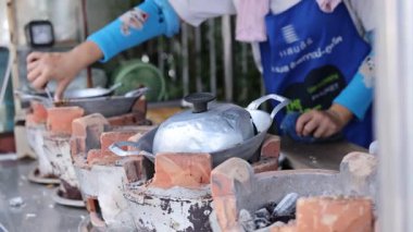 Bir satıcı, geleneksel Tayland hindistan cevizi aperatiflerini, kalabalık bir Phuket pazarında, yerel mutfak tekniklerini sergileyen kil sobalarla hazırlıyor.