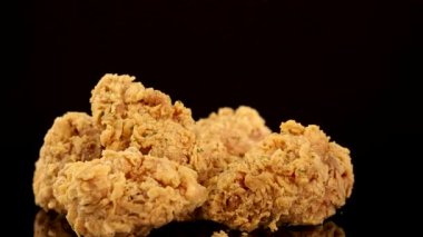 Altın renginde, kırışmış tavuk göğsü ve kalçaları dramatik bir stüdyo ışıklandırması ve koyu bir arkaplanı olan yansıtıcı bir yüzeyde yavaşça döner.