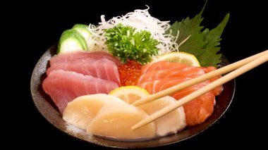 Çubuklar, parlak arka planda siyah bir zemin üzerinde somon, ton balığı, yumurta ve garnitürlü canlı bir suşiden deniz tarağı sashimi seçer.