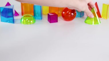 Bir el, beyaz bir zemin üzerinde canlı üç boyutlu geometrik şekillerle etkileşime girer, hareket ve dengeyi gösterir.