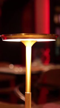 Bir el uzanır ve parlak, altın bir masa lambasının tepesine dokunur loş, ılık tonlu bir odada, LED ışığını etkinleştirir.