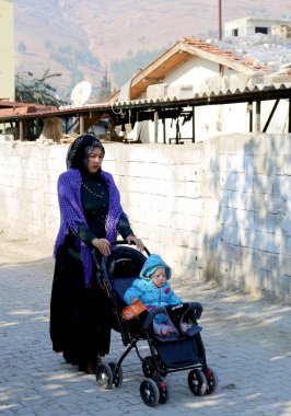 OVAKENT, HATAY, TURKEY-ARALIK 10 ARALIK: Stroller 'da oğlu olan kimliği belirsiz Özbek Kadın sokakta yürüyor. 10 Aralık 2016, Ovakent, Hatay, Türkiye