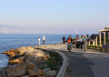 BUYUKADA, ISTANBUL, TURKEY-NOVEMBER 05, 2021: Kimliği belirsiz insanlar Deniz kenarında yürüyüş ve bisikletle güzel bir sonbahar gününün tadını çıkarıyor
