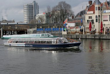 AMSTERDAM, NETHERLANDS-MARCH 01.2014: Amsterdam Turizm Ofisi 'nin yanında kimliği belirsiz yolcular, binalar ve tramvayla gezi teknesi