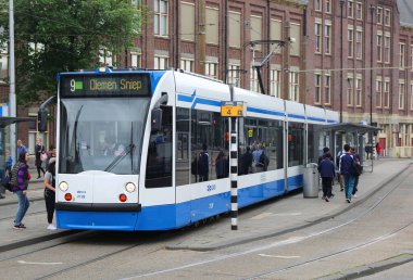 AMSTERDAM, NETHERLANDS-11 Haziran 2016: Kimliği belirsiz turistler Modern Tramvaya biniyor ve Amsterdam Centraal Tren Durağında yürüyor