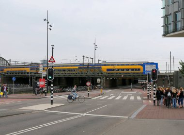 AMSTERDAM, NETHERLANDS-HAZİRAN 11 Haziran 2016: Amsterdam Centraal Tren İstasyonu 'na giden renkli trenin geçişi için kırmızı ışıkta bekleyen kimliği belirsiz kişiler