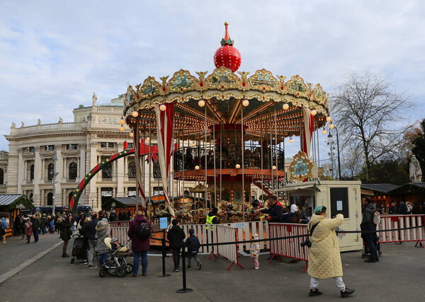 VIENNA, AUSTRIA-NOVEMBER 14,2023:Unidentified People visiting Christmas Market and Traditional Christmas Carousel aka Merry go round by the Historic Hofburg Theatre
