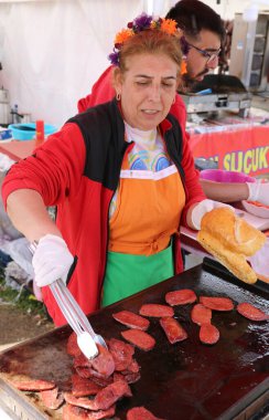 Adana, Türkiye-10 Nisan 2025: Kimliği belirsiz Kadın Aşçı Sucuk, nam-ı diğer Portakal Çiçeği Festivali 'nde Pepperoni Sandviçi pişiriyor