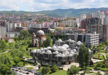 Priştine, Kosova-27 Mayıs 2025: Ulusal Kütüphane, Tamamlanmamış Sırp Kilisesi, Renkli Apartman Binaları ve Otoparkta yürüyen Tanımlanamayan İnsanlar 