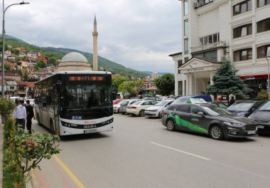 Prizren, Kosova-30 Mayıs 2025: Arkaplanda Sinan Paşa Camii ile Popular Hotel 'in önünden geçen halk otobüsü ve taksi