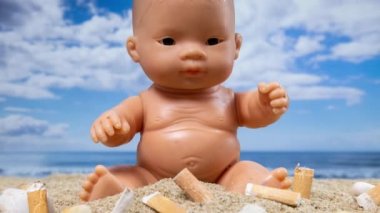 Güzel bir kumsalda sigarayla çevrili bir oyuncak bebek. 