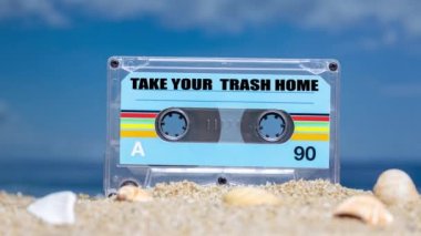 Plajda içinde kelimeler olan bir kaset. Çöpünü eve götür.