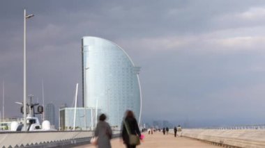 A timelapse view of people walking in port vell marina in barcelona with a stormy sky