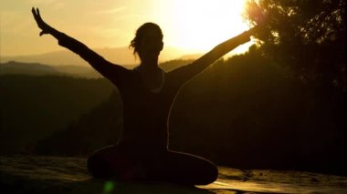 Gün batımında dağın tepesinde yoga yapan bir dişi. 