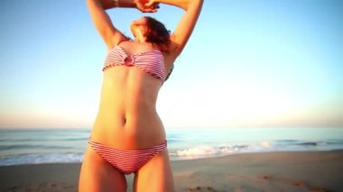 A beautiful woman in bikini dancing and posing on the beach 