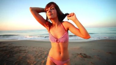 A beautiful woman in bikini dancing and posing on the beach 