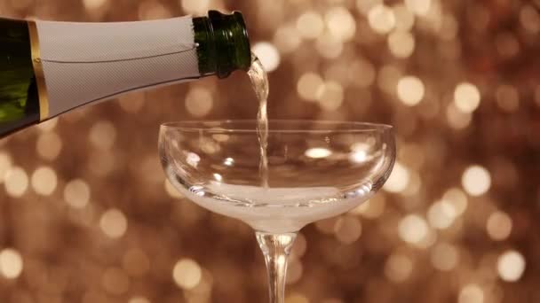 Champagne Gieten Een Glas Tegen Sprankelende Gouden Achtergrond — Stockvideo