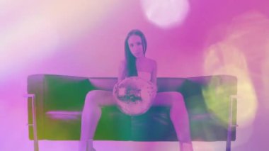 Beautiful female seated on sofa holding discoball