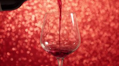 Pouring red wine into a glass with red sparkling background