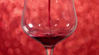 Pouring red wine into a glass with red sparkling background