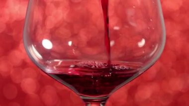 Pouring red wine into a glass with red sparkling background