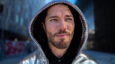 Gümüş kapüşonlu genç bir adam arka planda ofis binalarına bakıyor.