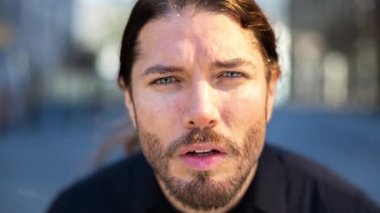 Arka planda ofis binaları olan ve kameraya yaslanan genç bir adam.