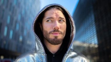 Gümüş kapüşonlu genç bir adam arka planda ofis binalarına bakıyor.