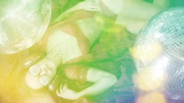 Disko kadını altın kristal güneş gözlükleriyle poz veriyor, altın disko toplarıyla çevrili.