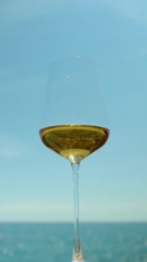  Güneşin doğuşunda ya da batışında arka planda beyaz şarap ve köpüklü deniz ve gökyüzü olan bir bardak.