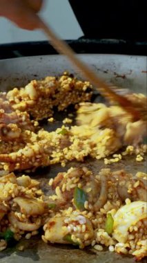 Şef metal tavada bileşenleri karıştırıyor, geleneksel İspanyol enginarlı paella yapıyor.