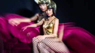 Güzel bir parti kadını altın kaskla kırmızı koltuğa oturmuş poz veriyor.