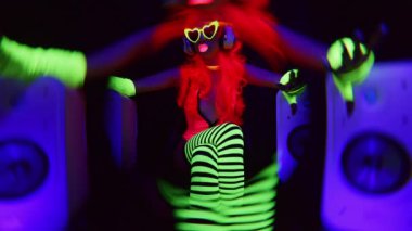 Ultraviyole floresan giyinen ve hoparlörlü makyaj yapan havalı dans eden bir kadın.