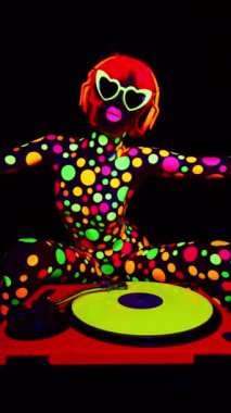 Havalı bir DJ kadın UV floresan giyiniyor ve dikey makyaj yapıyor.