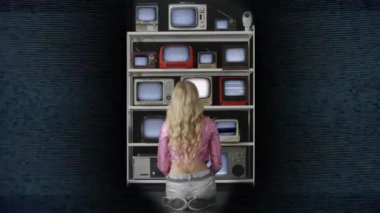 Arızalı televizyon ekranlarından oluşan duvarı arkadan izleyen bir kadın. 