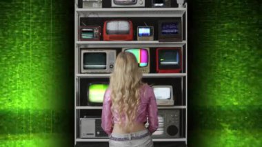 Arızalı televizyon ekranlarından oluşan duvarı arkadan izleyen bir kadın. 