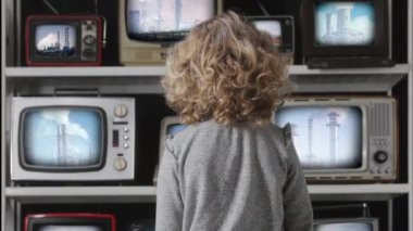 Genç kız ekranlarında elektrik santrallerinin videoları olan bir televizyon bankasını izliyor. 