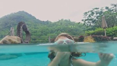 Palmiye ağaçlarının yemyeşil kırsalında lüks bir yüzme havuzunda oynayan küçük kız. 