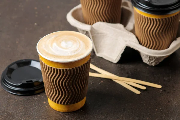 Paper cups with cappuccino on a stand on a brown table. coffee to go