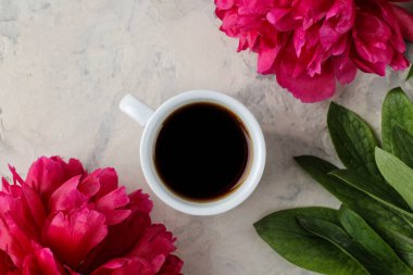 Frame of beautiful bright pink peony flowers and a cup of coffee on a light background. top view.