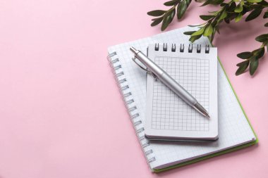 Narin pembe arka planda yeşil yapraklı ve kalemli defterler. en üstteki görünüm